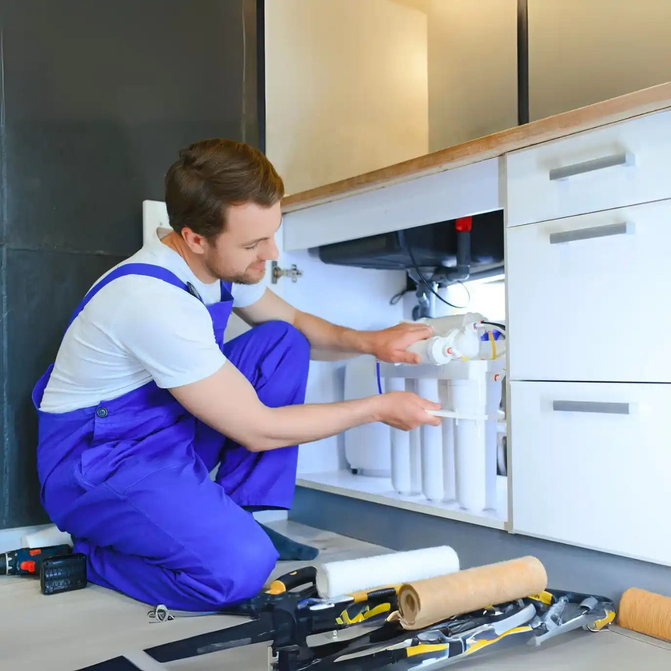 Person in blue overalls working on a kitchen sink installation.