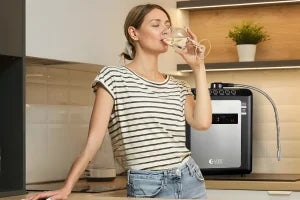 Woman drinking water from a glass in a kitchen with a water filter system.