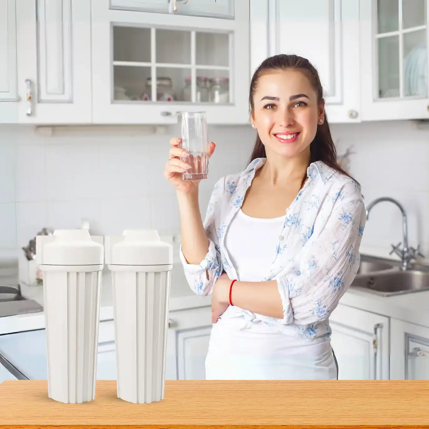 Woman holding a glass of water in a kitchen with water filters on the counter.
