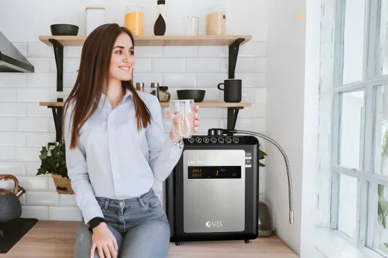 Woman holding a glass of water next to an oxygen Life Ionizer Water Purifier in a kitchen.