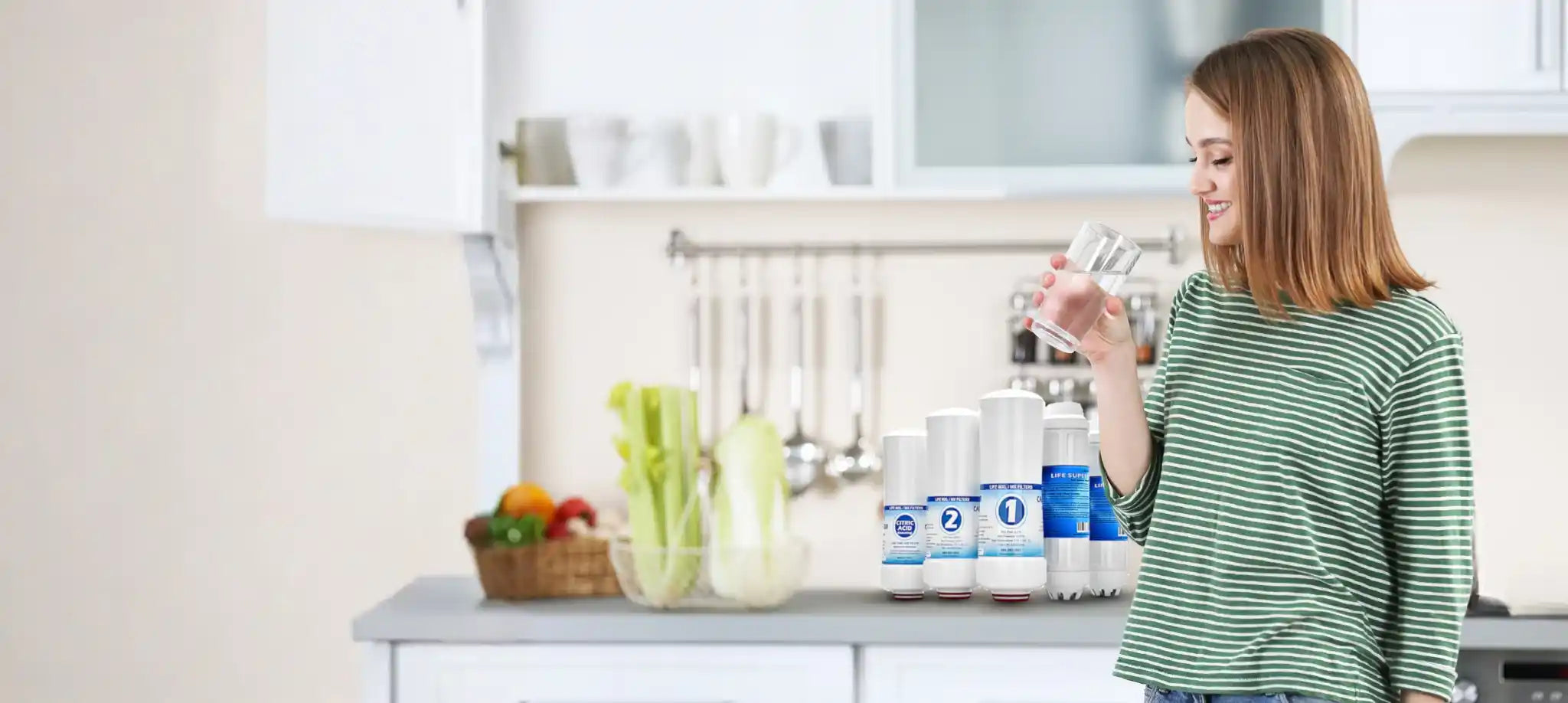 Woman in a kitchen holding a container of yogurt with various yogurt containers and fruits on the counter.