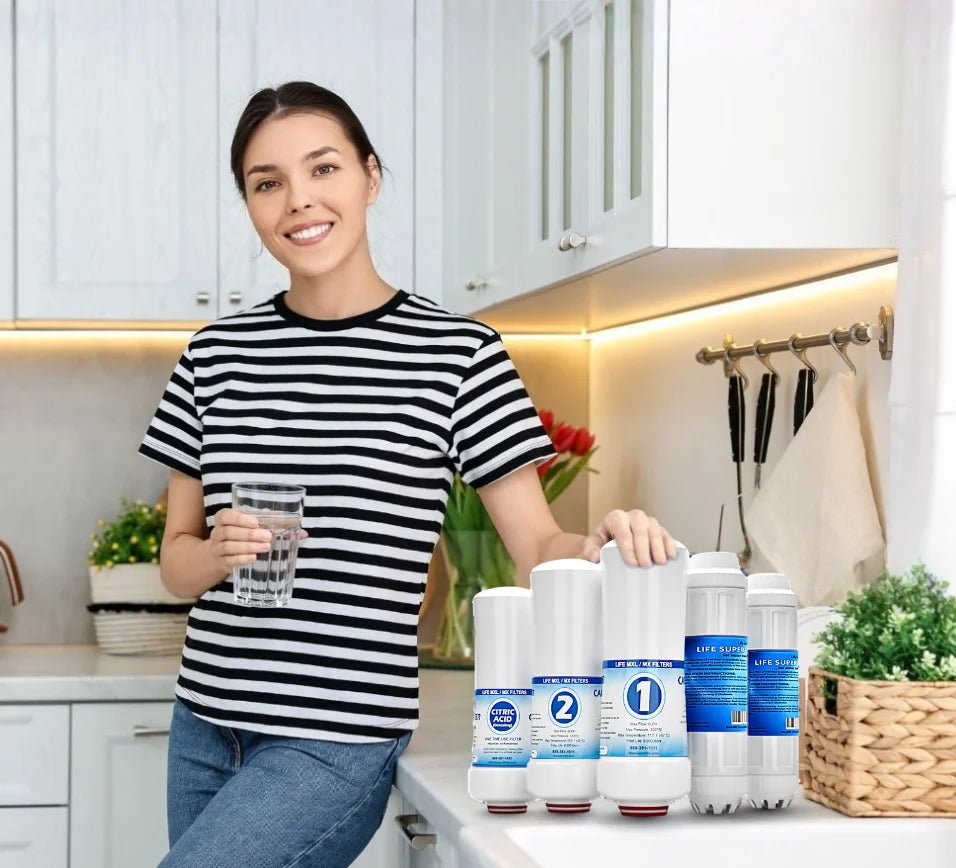 Woman holding a glass of water with a row of Life Ionizer water Filters on a kitchen counter.